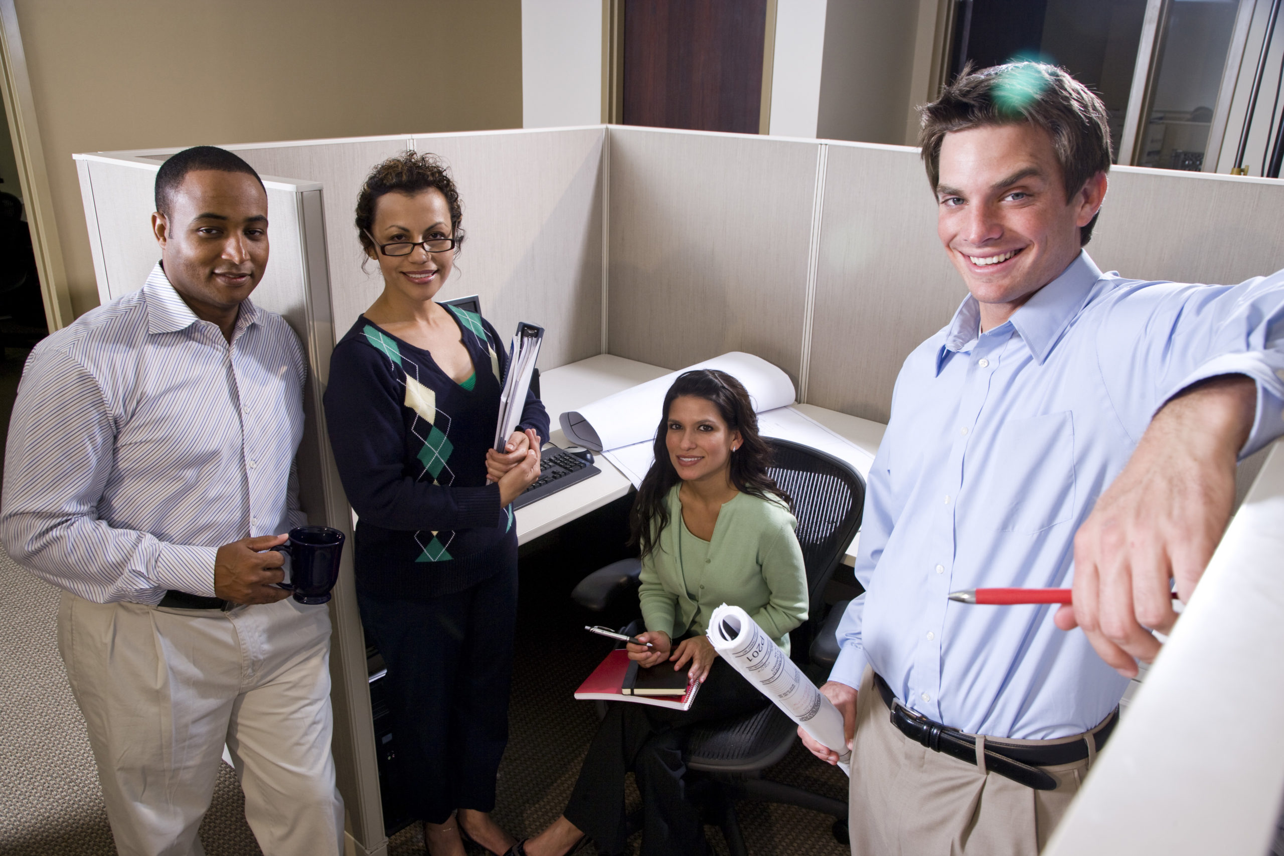 three people standing in an office cubicle holding pens and paper