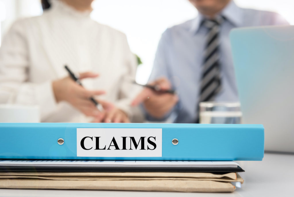 two people sitting at a desk with a binder that says claims