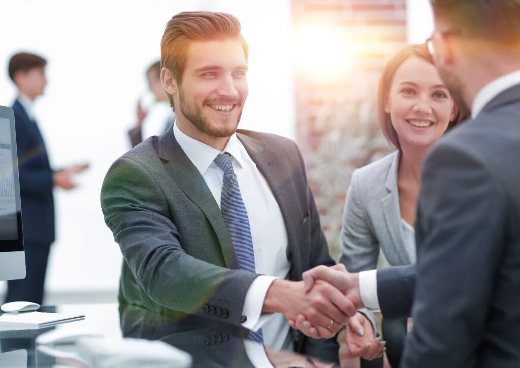 two business people shaking hands in front of a computer screen