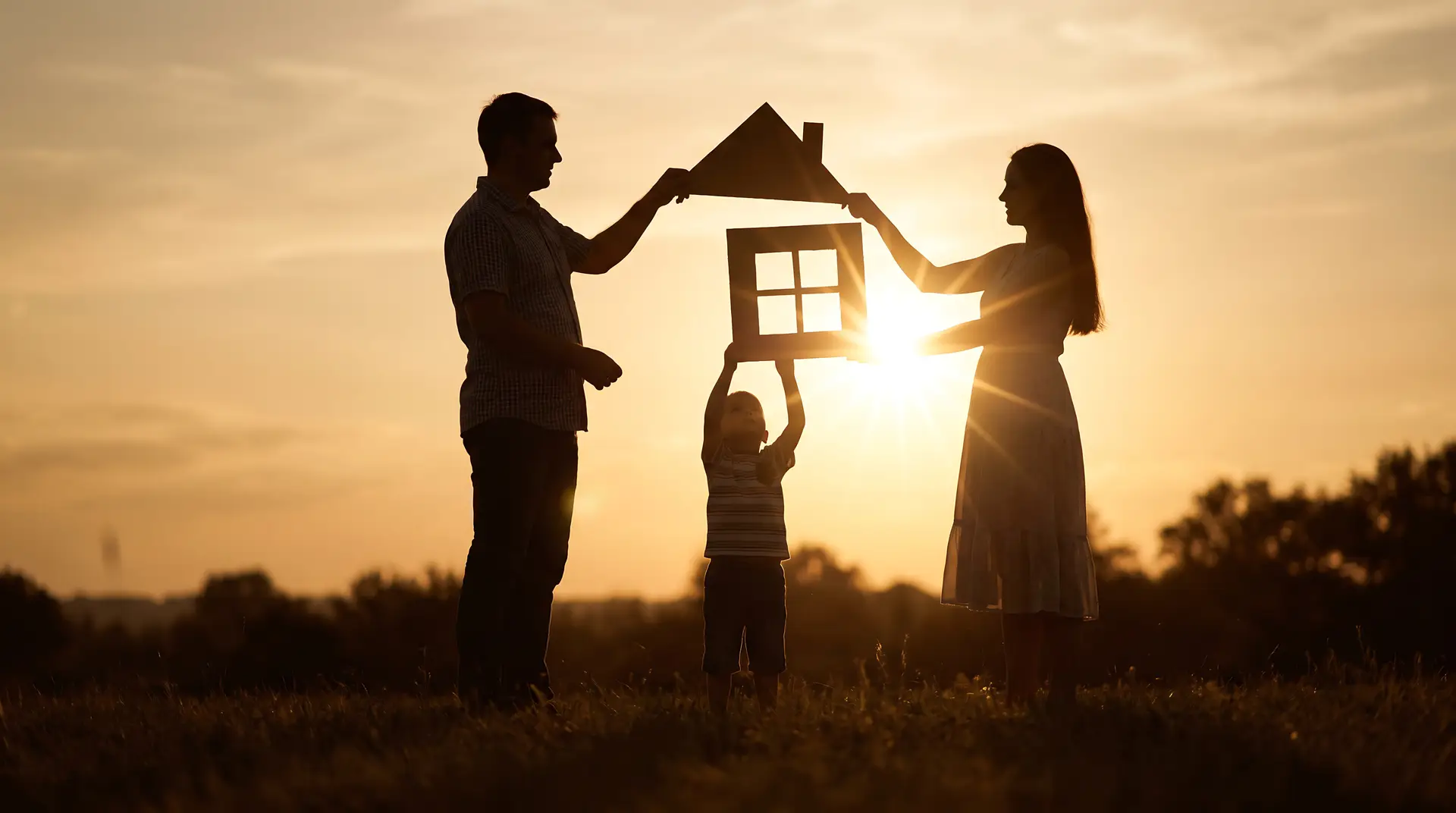 family silhouette holding a house shape at sunset