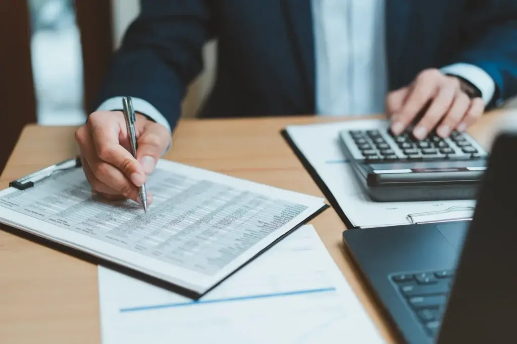 Professional reviewing a fee spreadsheet with a calculator and laptop