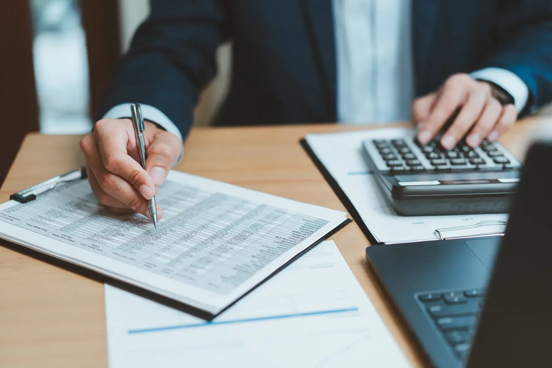 Professional reviewing a fee spreadsheet with a calculator and laptop